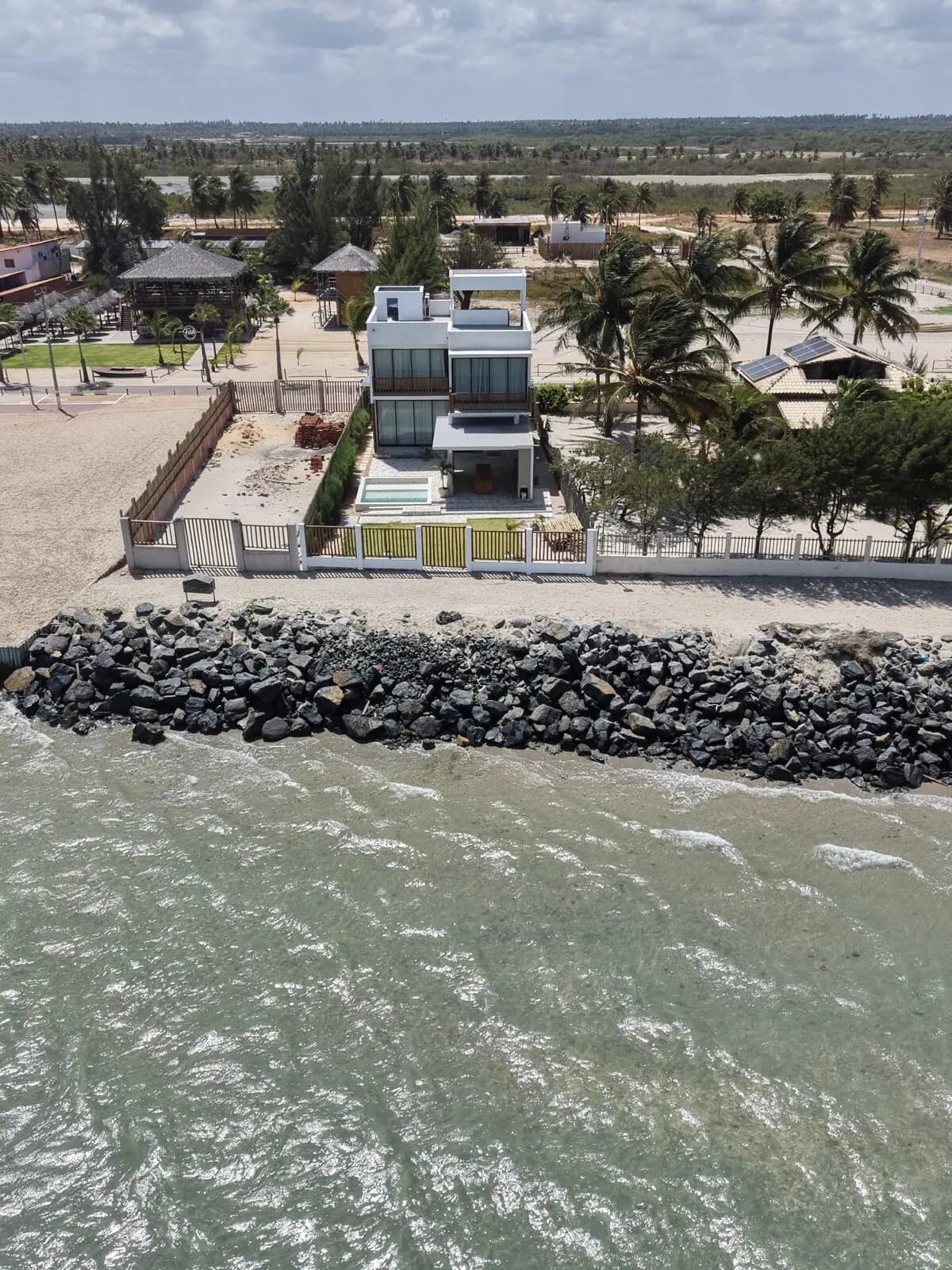 Vista aérea da casa e do enrocamento de pedras que separa a casa do mar