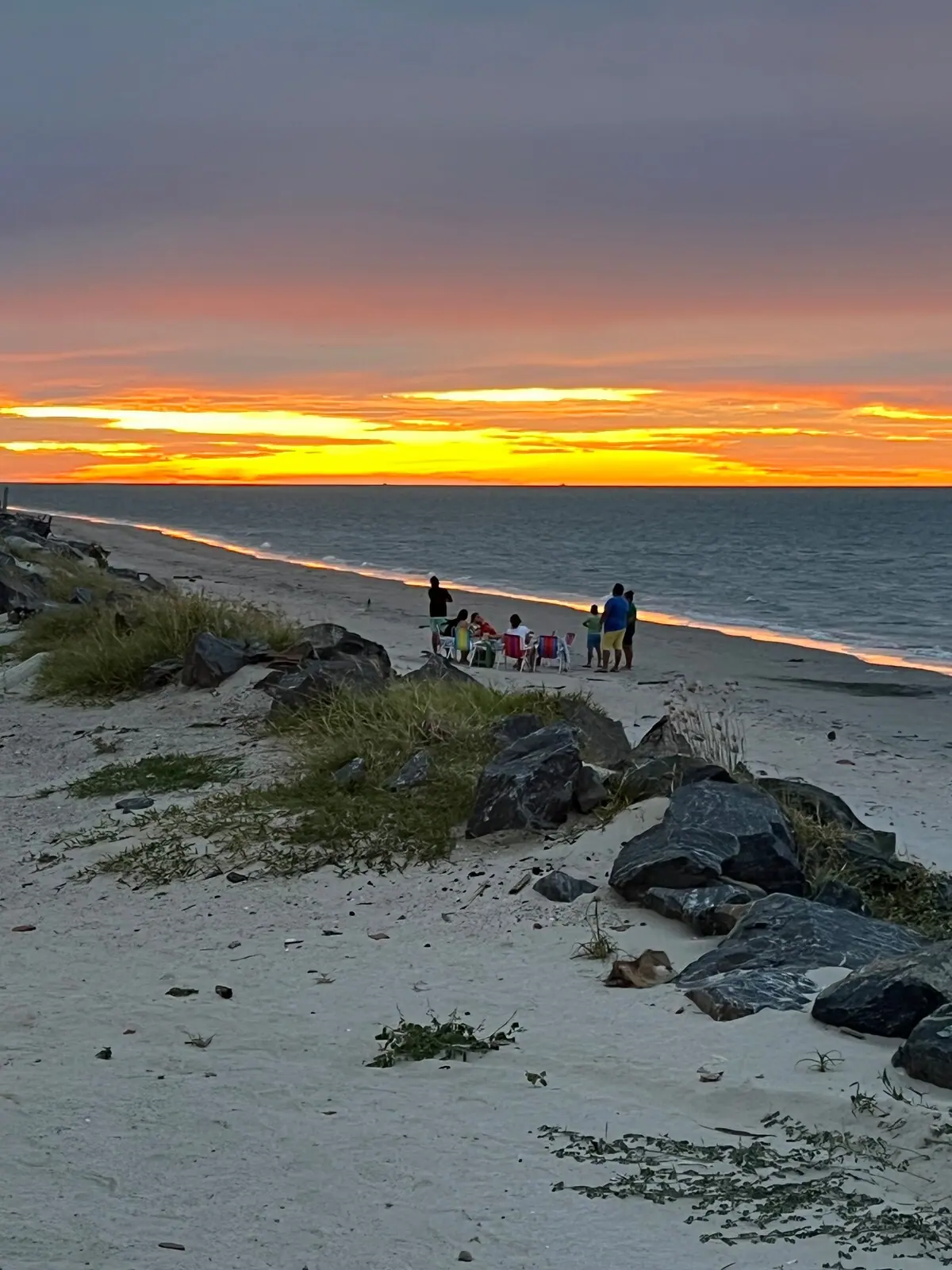 Faixa de areia e pedras com o céu laranja no fim do dia