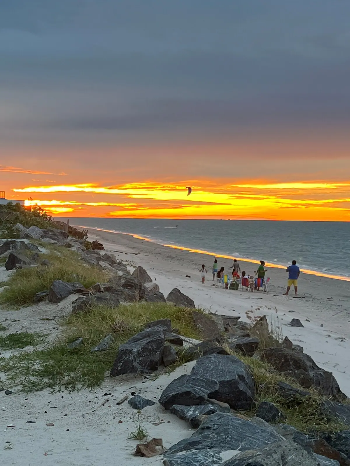 Pôr do sol alaranjado na praia, com pessoas caminhando na areia