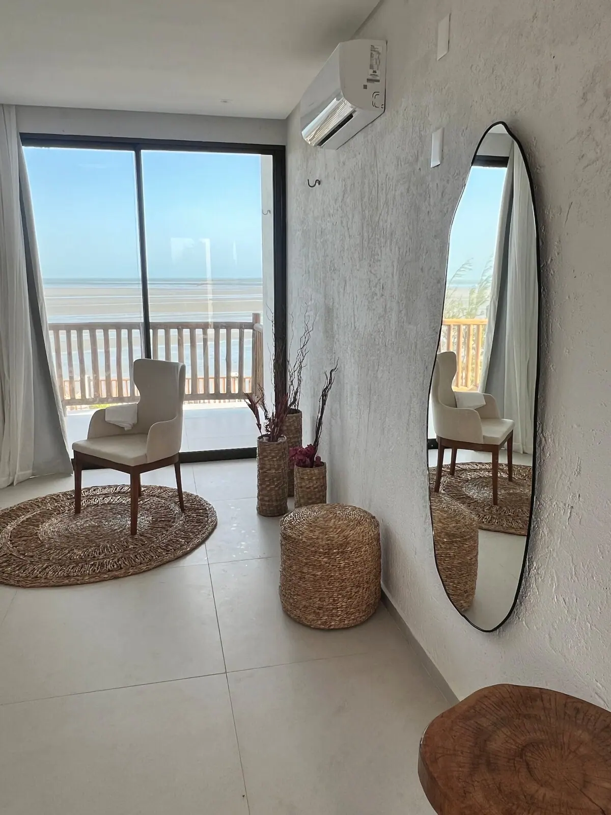 Quarto com espelho redondo, poltrona e vista para a praia