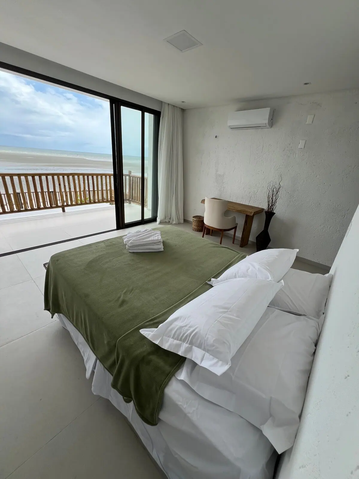 Quarto com cama, mesa e porta de vidro com vista para o mar