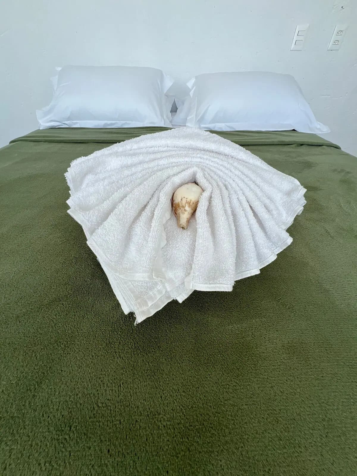 Cama com manta verde e toalha dobrada com uma concha