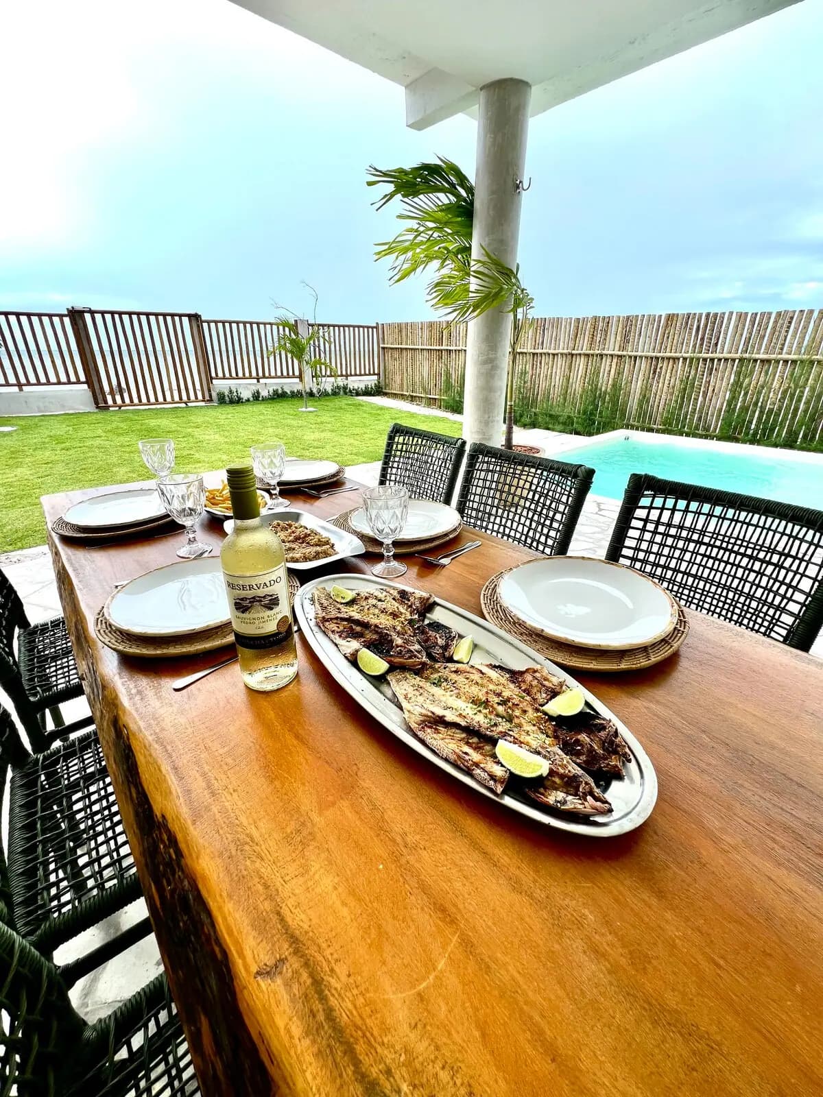 Mesa posta com peixe assado, taças e a piscina ao fundo