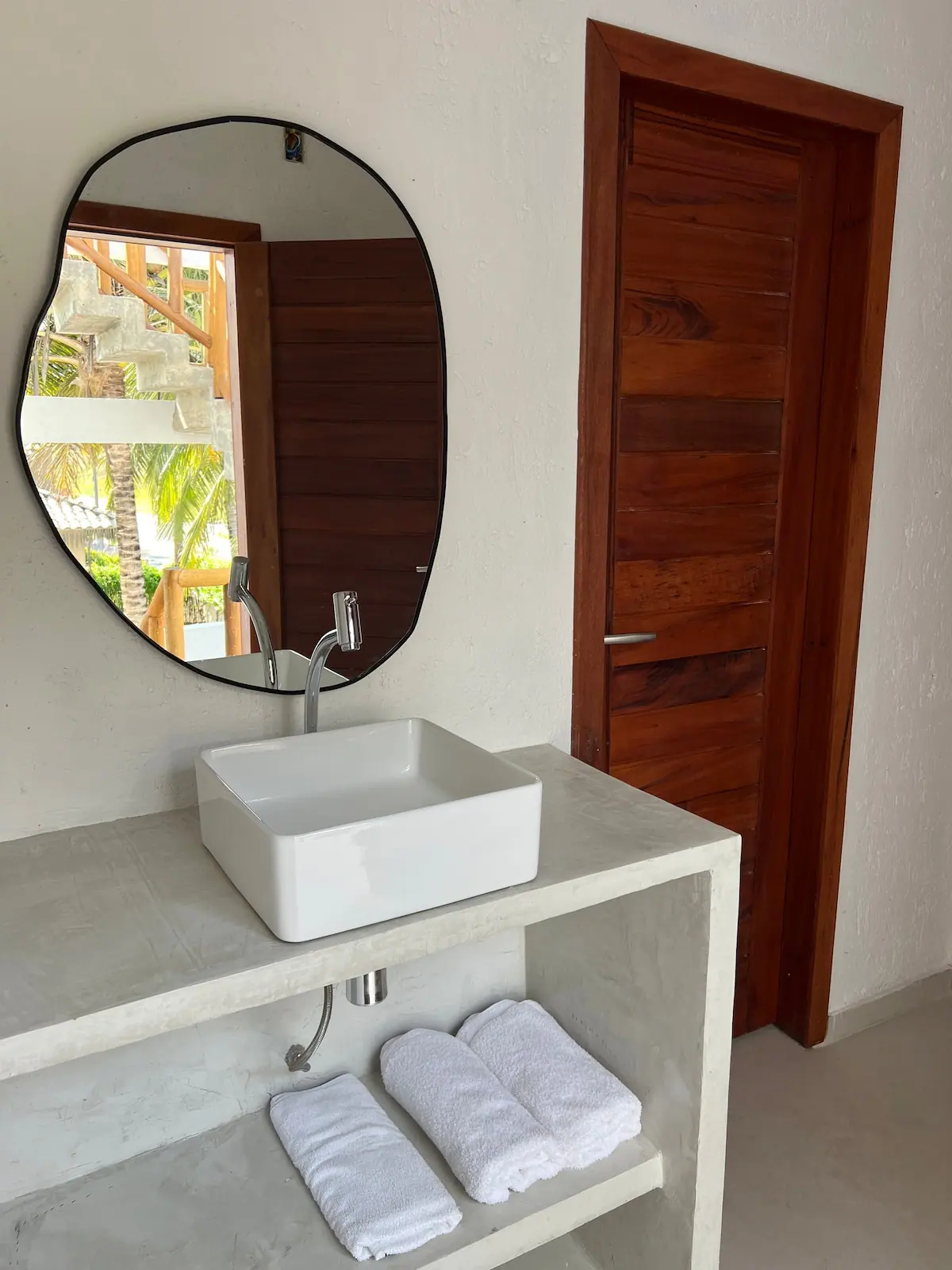 Banheiro com cuba de apoio, espelho orgânico e porta de madeira