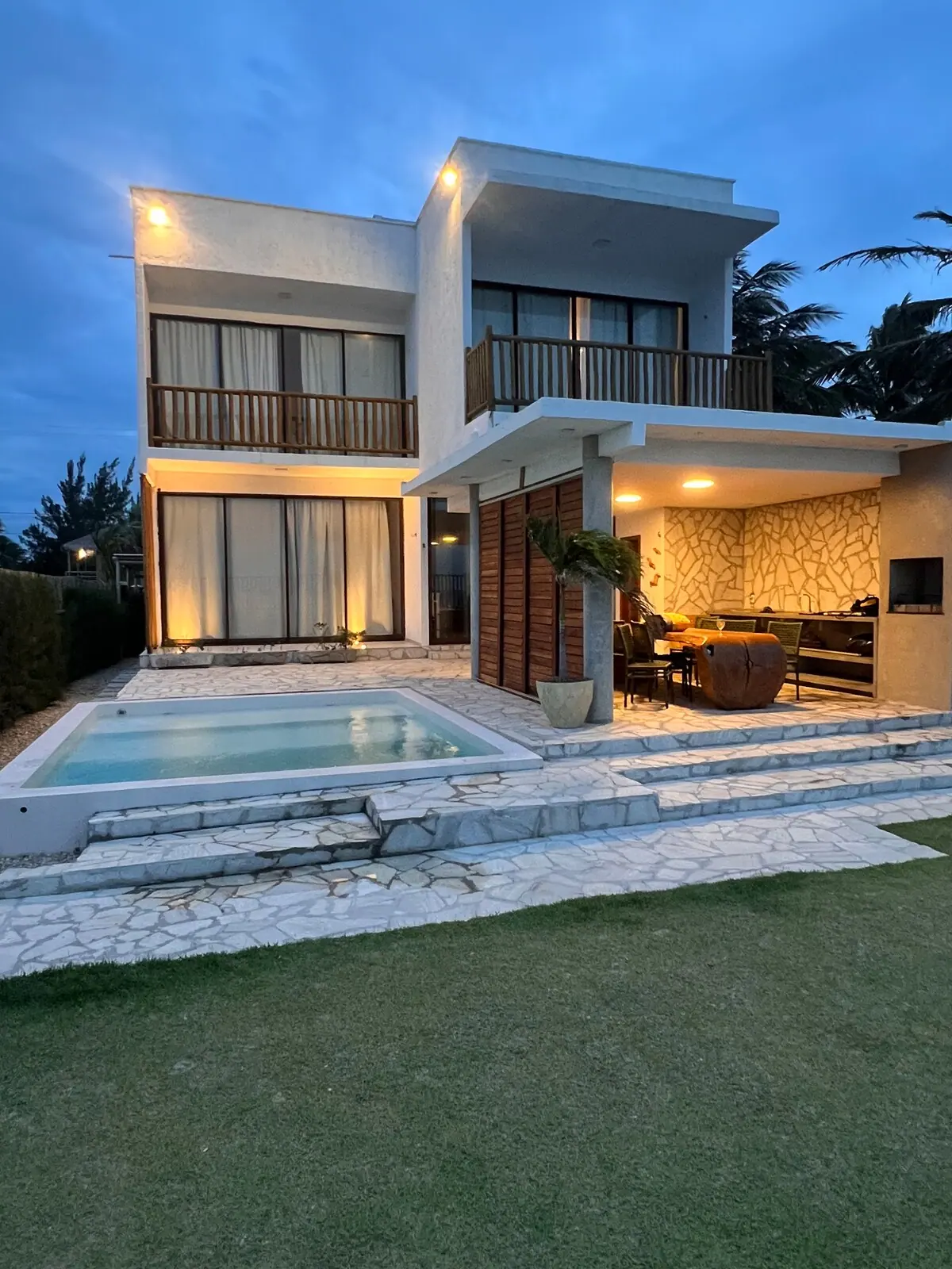 Fachada da Casa Ventus ao entardecer, com a piscina iluminada e o gramado em primeiro plano