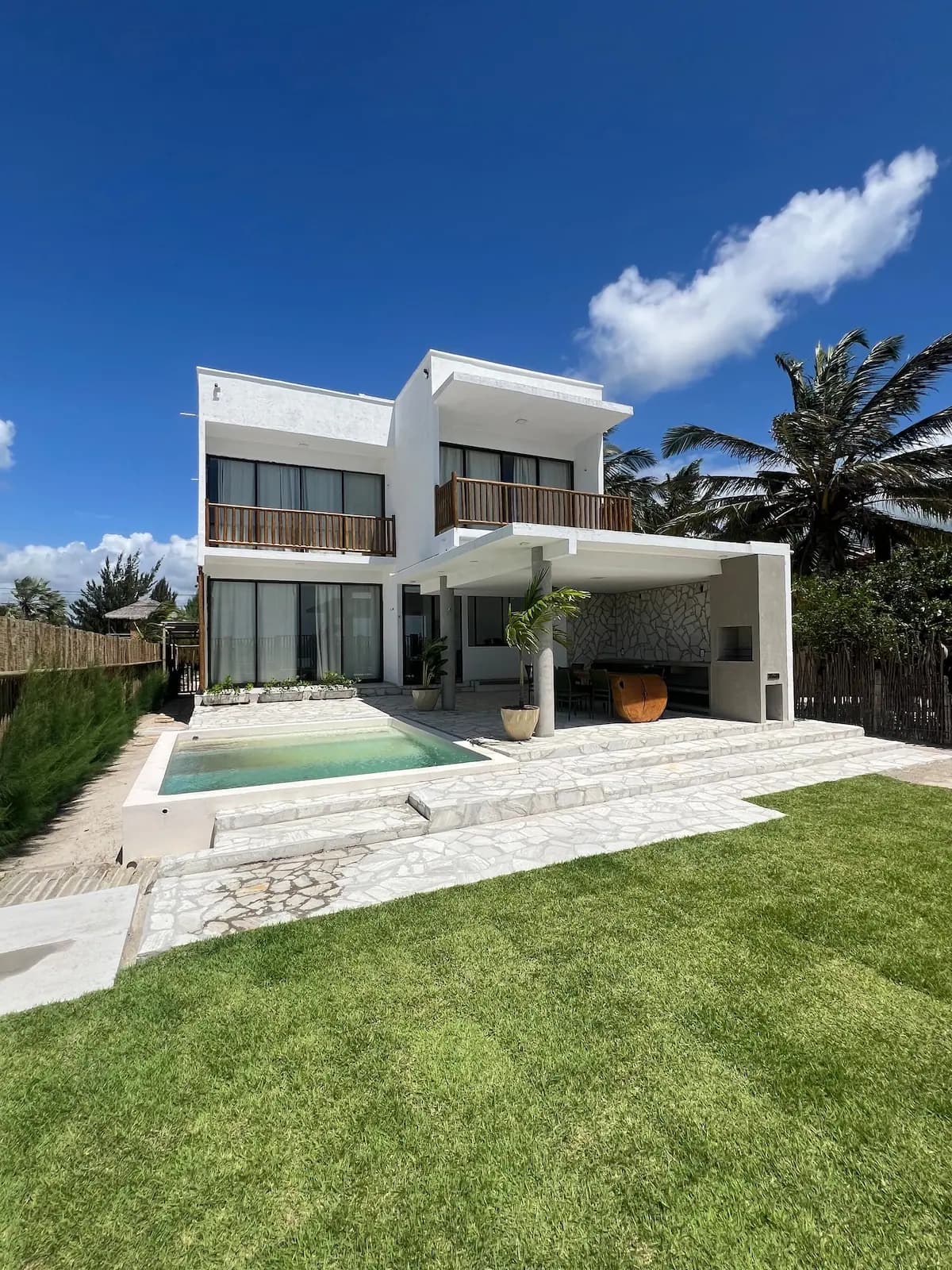 Casa Ventus de dia, dois andares brancos com varandas de madeira e gramado à frente