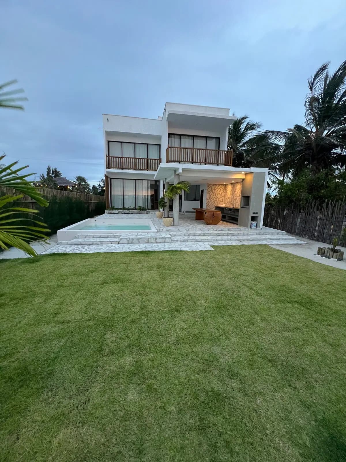 Fachada da casa vista do gramado, com a área coberta e a piscina ao fundo