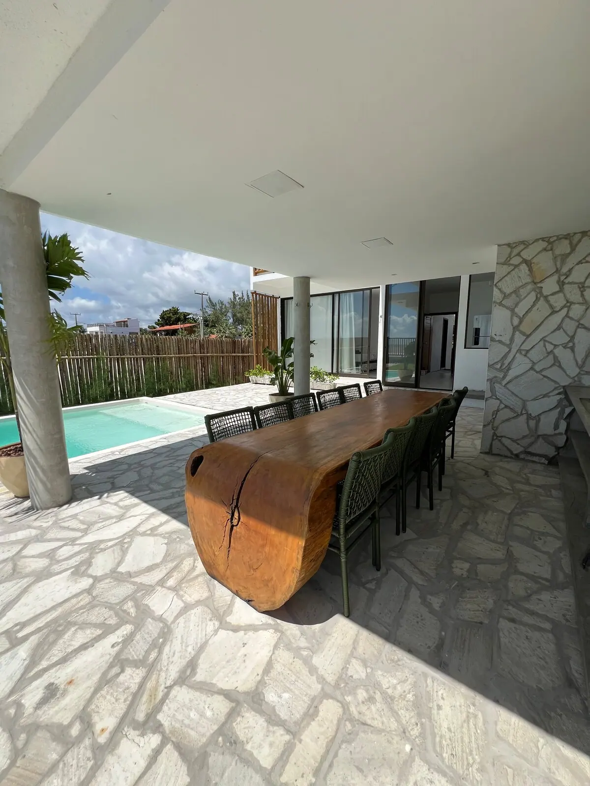 Área coberta com a mesa longa de madeira e a piscina ao lado