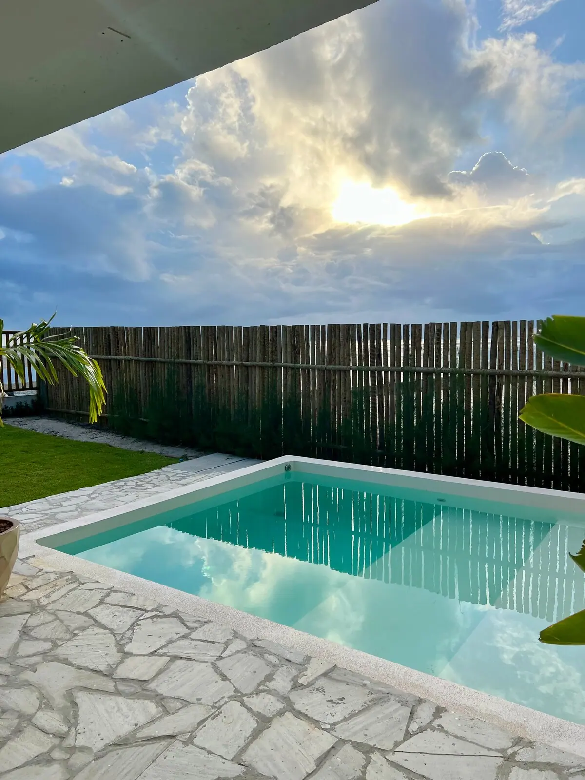 Piscina de água clara ao lado da cerca de bambu, com nuvens ao fundo