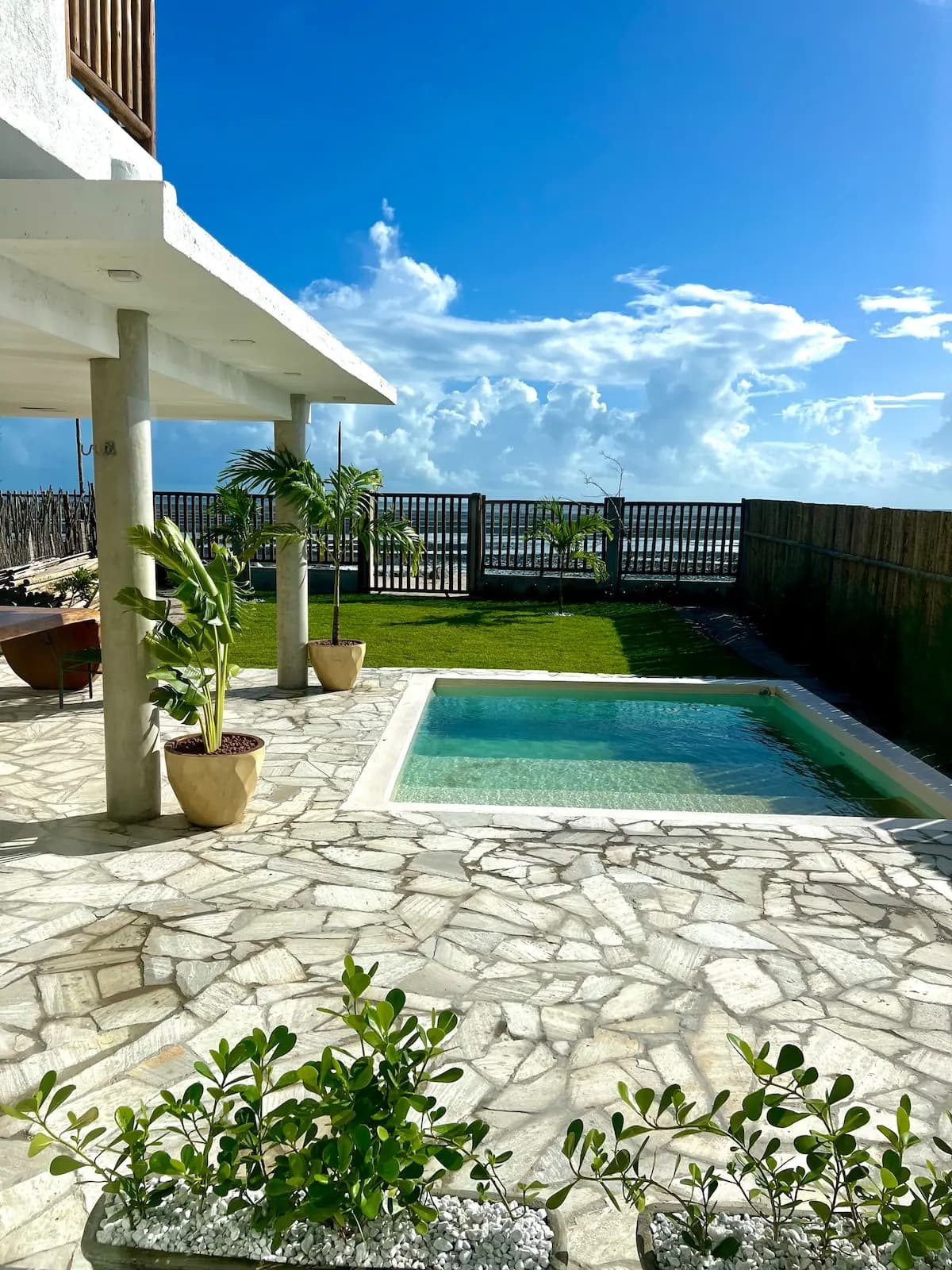 Piscina e deck de pedra com plantas, sob céu azul